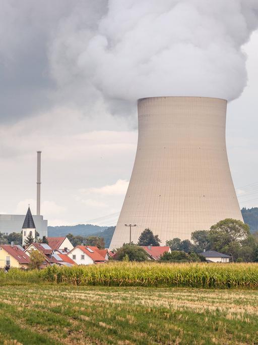 Der dampfende Kühlturm des Kernkraftwerks Isar 2 in Bayern, im Vordergrund das Dorf Wattenbacherau mit Ziegeldächern und Kirchturm