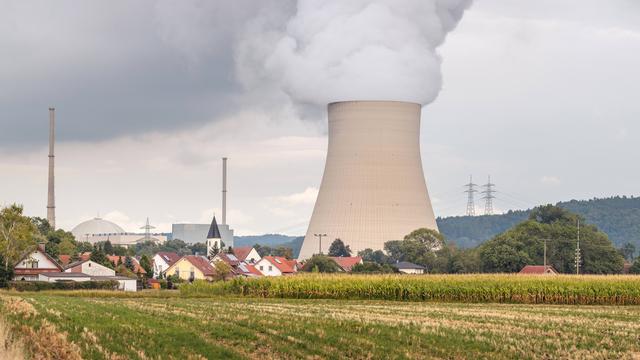 Der dampfende Kühlturm des Kernkraftwerks Isar 2 in Bayern, im Vordergrund das Dorf Wattenbacherau mit Ziegeldächern und Kirchturm.