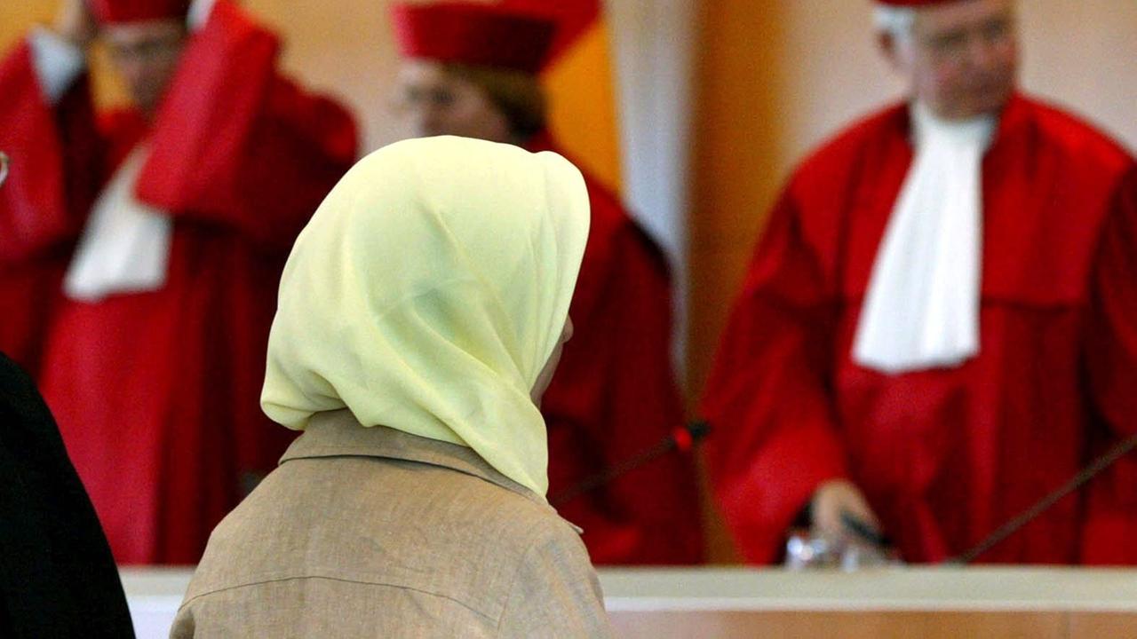 Eine Frau mit Kopftuch sitzt in einem Saal im Bundesverfassungsgericht. Eine Frau mit Kopftuch sitzt in einem Saal im Bundesverfassungsgericht.