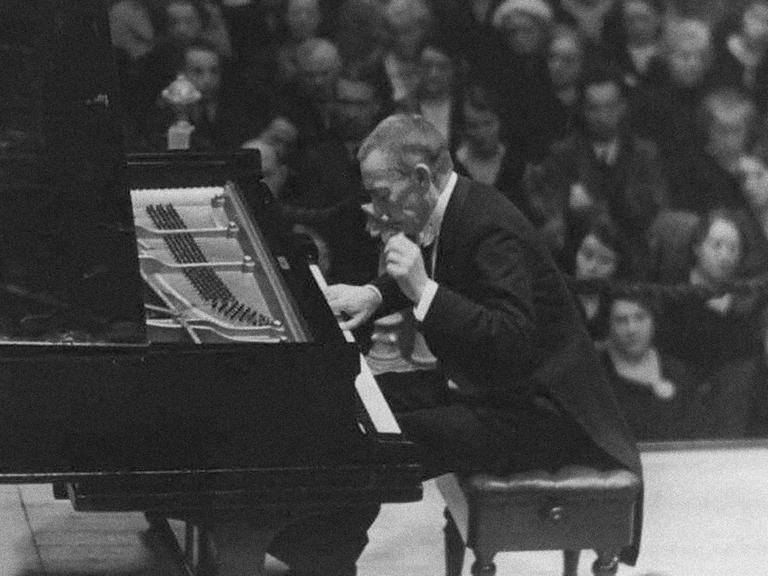 Auf dem Bild ist ein Mann im Anzug zu sehen, der ein Konzert an einem Klavier gibt. 