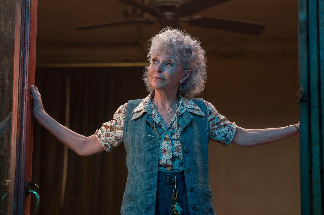 Rita Moreno steht an einem Fenster und blickt schräg nach oben. Rita Moreno steht an einem Fenster und blickt schräg nach oben.