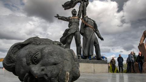 Zwei Statuen halten einen Sowjetstern in ihren Händen. Der rechten fehlt der Kopf, er liegt vor ihnen auf dem Boden.