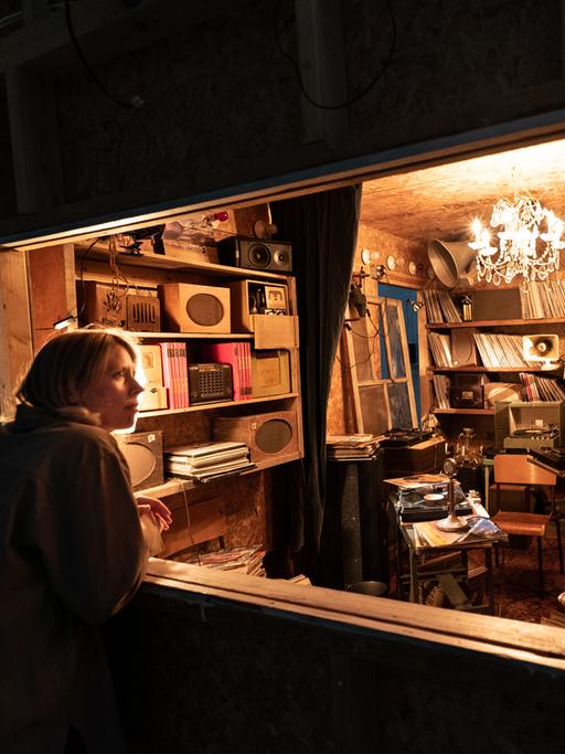 Eine Frau schaut durch ein Schaufenster in einen kleinen mit Schallplatten und Archivalien vollgestopften Raum