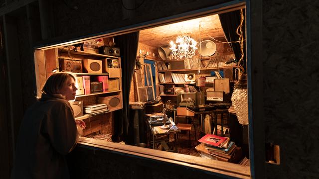 Eine Frau schaut durch ein Schaufenster in einen kleinen mit Schallplatten und Archivalien vollgestopften Raum