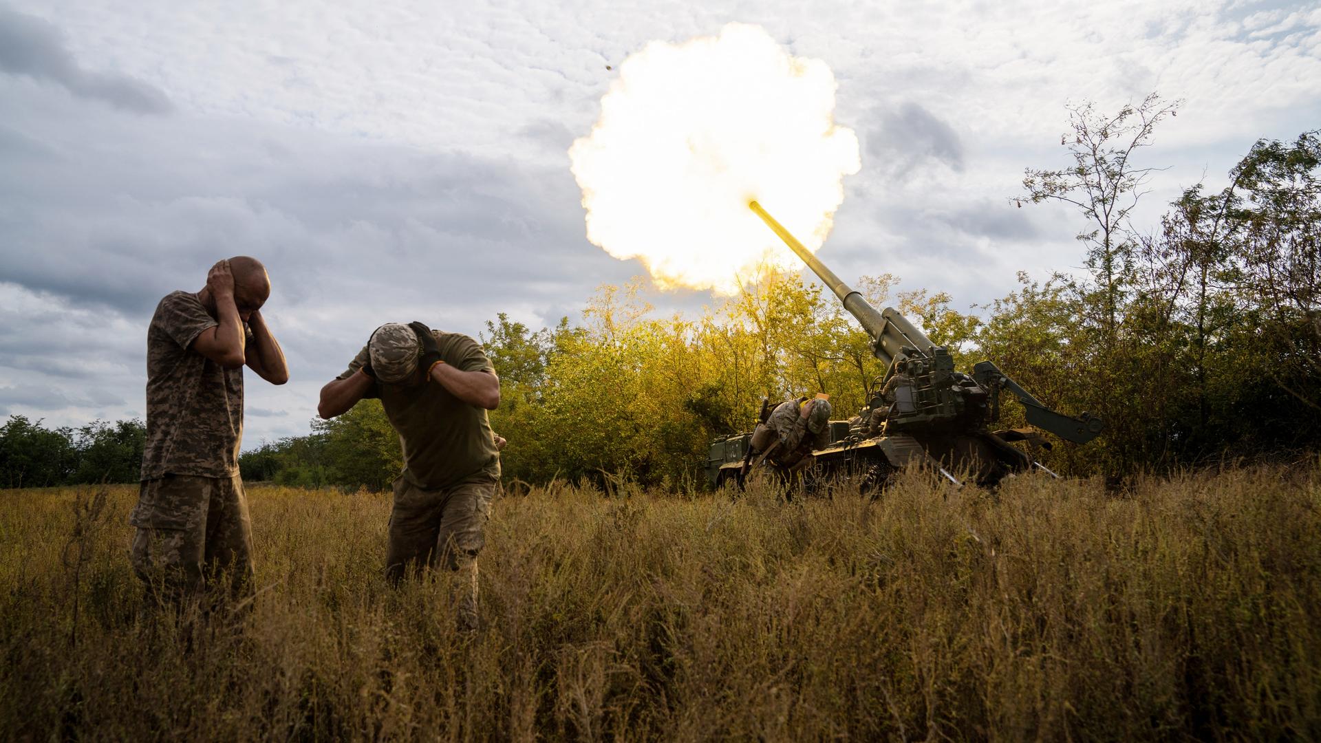Ukrainische Soldaten feuern an der südlichen Frontlinie der Ukraine am 15. September 2022. Zwei Soldaten gehen in Deckung und halten sich die Ohren zu. Eine Rauchsäule steigt auf.