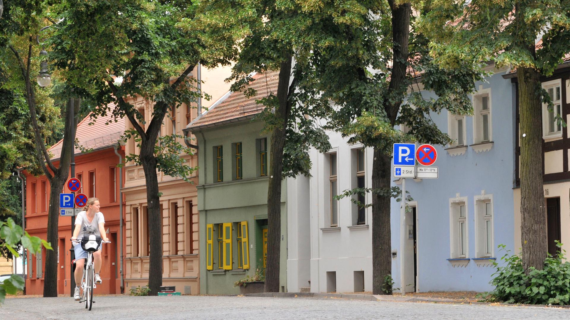 Eine Radfahrerin fährt durch eine Dorfstraße mit bunten Häusern in Brandenburg Eine Radfahrerin fährt durch eine Dorfstraße mit bunten Häusern in Brandenburg