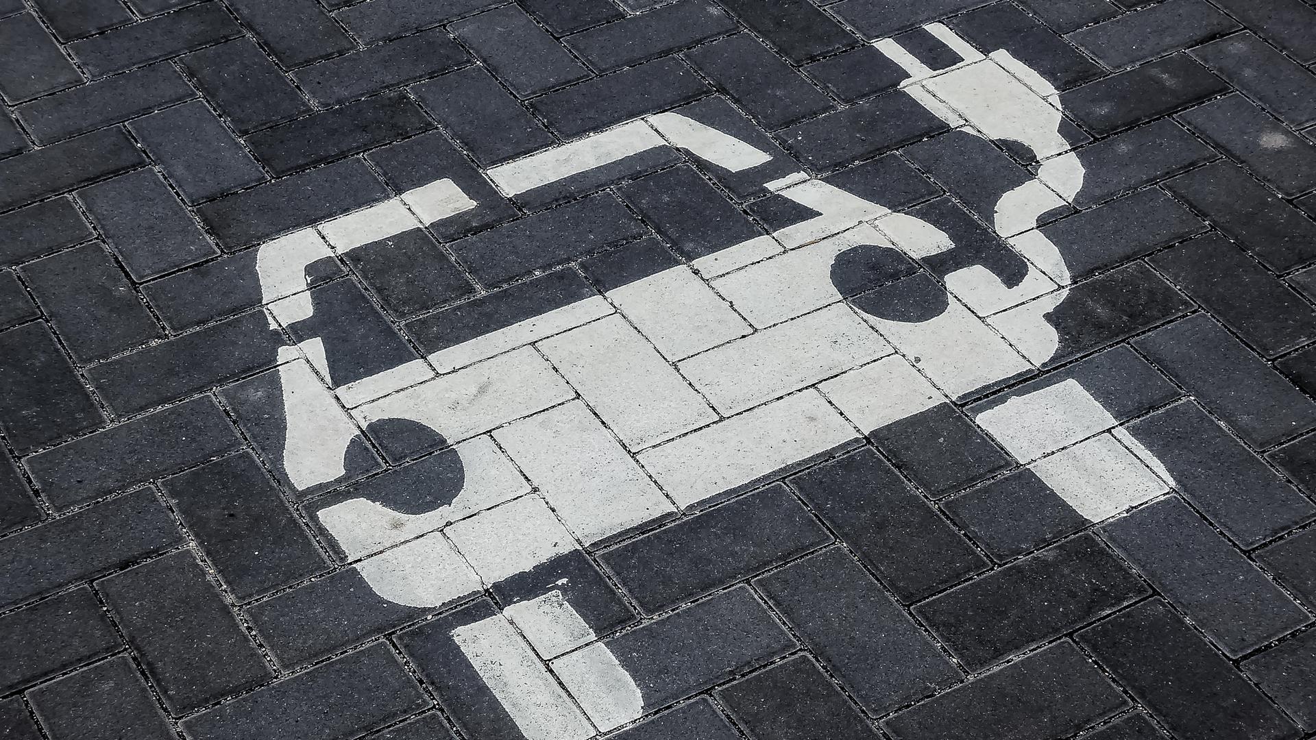 Ein Parkplatz für Elektroautos. Auf die Pflastersteine ist in Weiß ein Elektrofahrzeug mit Ladekabel gemalt. Ein Parkplatz für Elektroautos. Auf die Pflastersteine ist in Weiß ein Elektrofahrzeug mit Ladekabel gemalt.