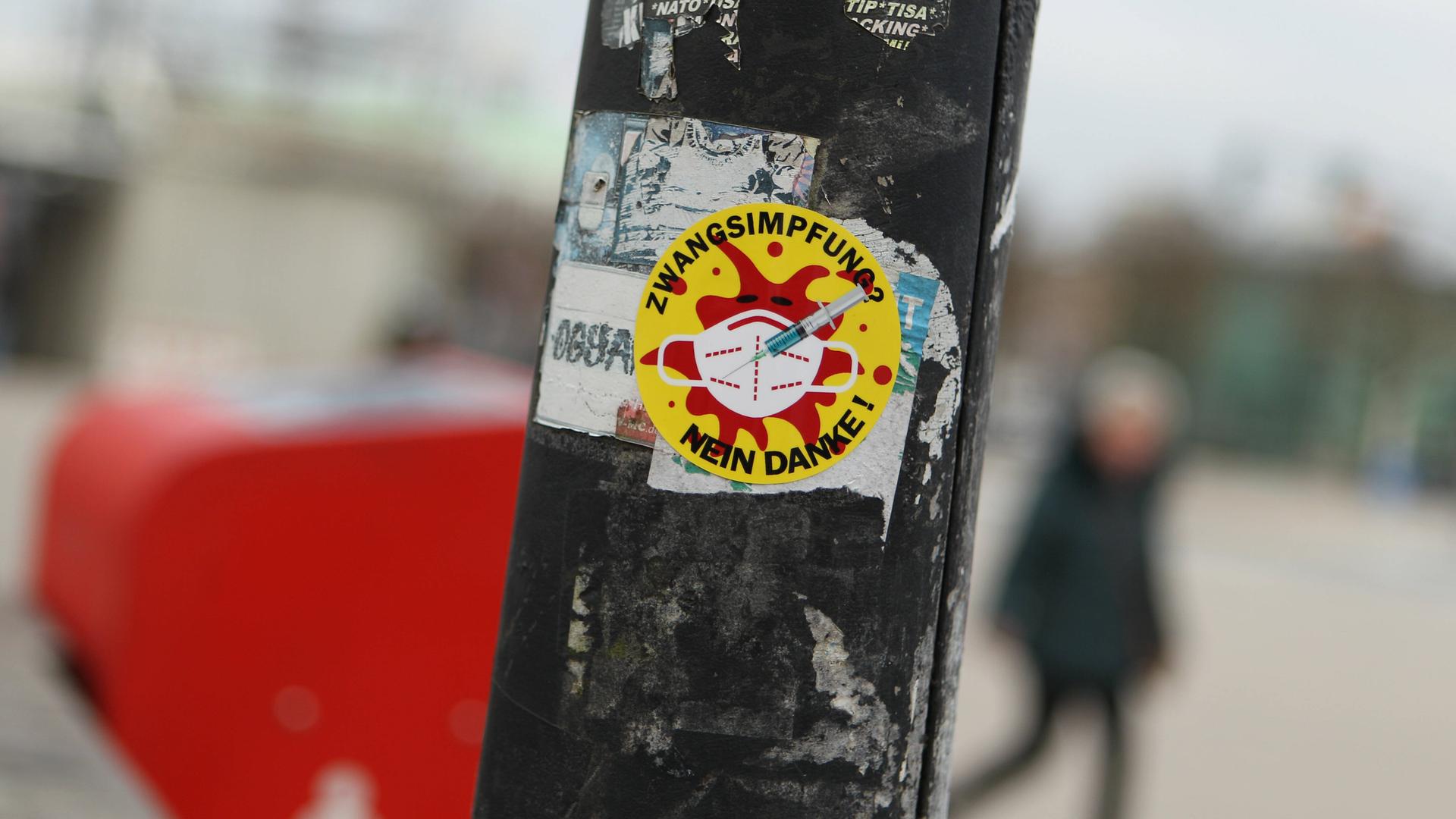 Sticker an einem Laternenpfahl, auf dem steht "Zwangs-Impfung? Nein danke". Das Motiv, ein rotes Coronavirus auf gelben Grund, erinnert an die Anti-Atomkraft-Aufkleber mit dem Text "Atomkraft? Nein danke". Sticker an einem Laternenpfahl, auf dem steht "Zwangs-Impfung? Nein danke". Das Motiv, ein rotes Coronavirus auf gelben Grund, erinnert an die Anti-Atomkraft-Aufkleber mit dem Text "Atomkraft? Nein danke".