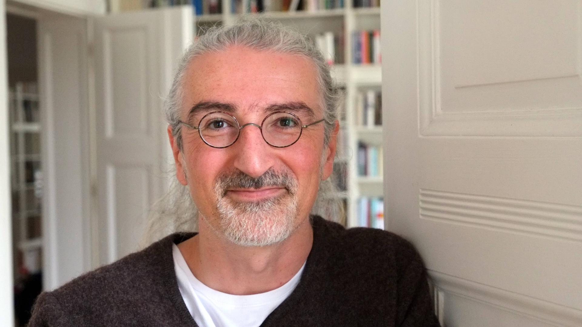 Porträtfoto des Schriftstellers Zoran Drvenkar, im Hintergrund sind weißgestrichene Türen und Bücherregale zu sehen. 