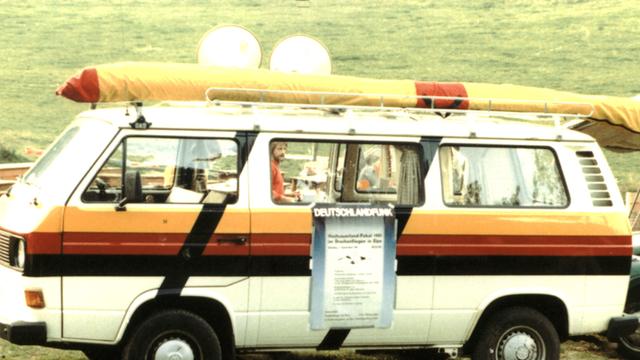 Ein VW-Bus mit einem aufgeklebten Deutschlandfunk-Plakat steht auf einer Wiese in Elspe, 1981 Ein VW-Bus mit einem aufgeklebten Deutschlandfunk-Plakat steht auf einer Wiese in Elspe, 1981