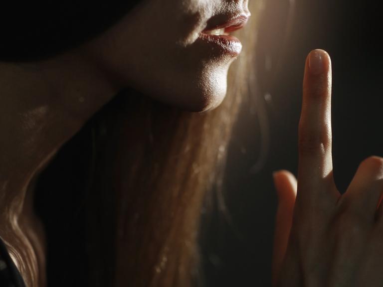 Eine Frau deutet mit dem Finger vor dem Mund ein Geheimnis an.