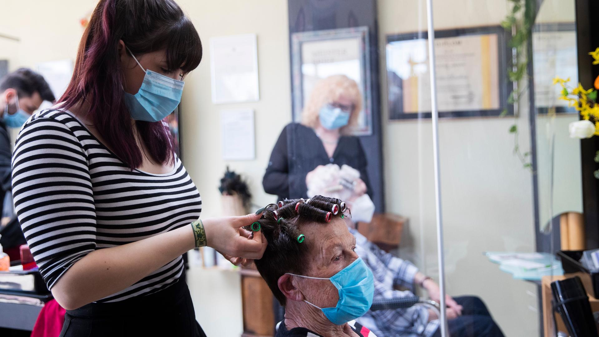 Eine Friseurin in einem Friseursalon nimmt einer Kundin Lockenwickel aus den Haaren. Eine Friseurin in einem Friseursalon nimmt einer Kundin Lockenwickel aus den Haaren.