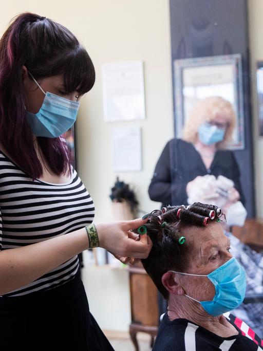 Eine Friseurin in einem Friseursalon nimmt einer Kundin Lockenwickel aus den Haaren.