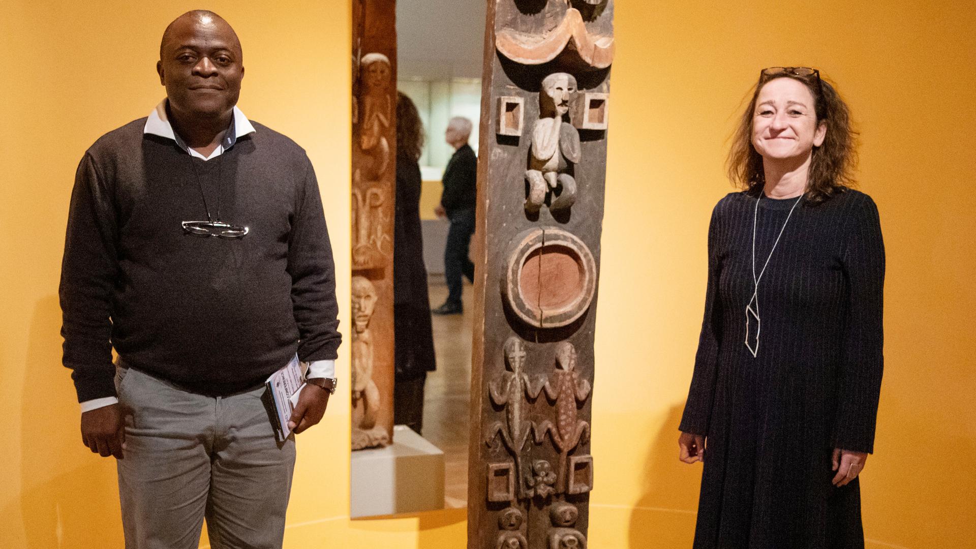 Karin Guggeis, Projektleitung des Museums, steht in der Ausstellung vom Museum Fünf Kontinente neben Albert Gouaffo, Projektkoordinator der Universität Dschang (Kamerun), neben dem "Blauen-Reiter Pfosten". 