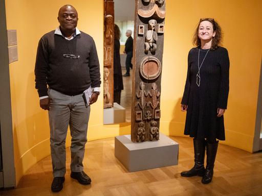 Karin Guggeis, Projektleitung des Museums, steht in der Ausstellung vom Museum Fünf Kontinente neben Albert Gouaffo, Projektkoordinator der Universität Dschang (Kamerun), neben dem "Blauen-Reiter Pfosten". 