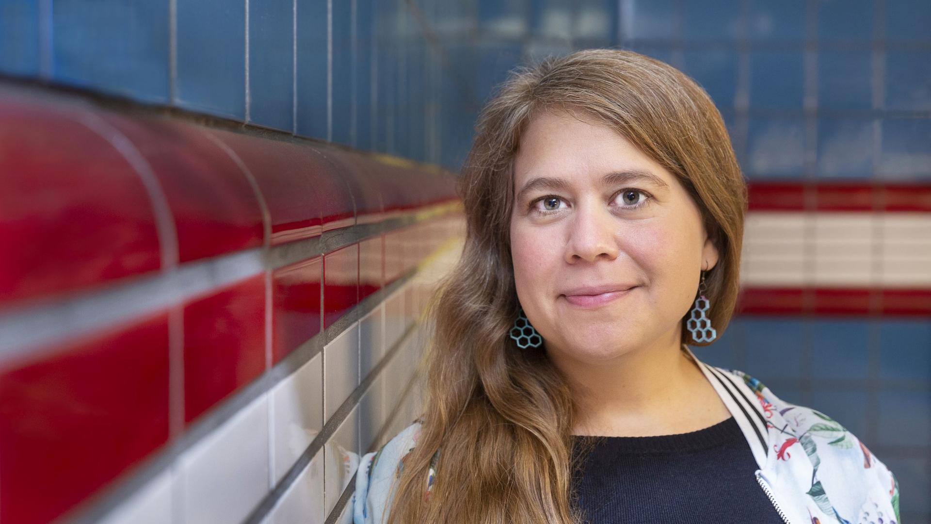 Julia von Lucadou steht angelehnt an eine Fliesenwand, im Hintergrund ist auch eine Fliesenwand. Sie hat lange Haare, die sie mir Seitenscheitel trägt. Ihre Jacke ist hell, ihr T-Shirt dunkelblau. Julia von Lucadou steht angelehnt an eine Fliesenwand, im Hintergrund ist auch eine Fliesenwand. Sie hat lange Haare, die sie mir Seitenscheitel trägt. Ihre Jacke ist hell, ihr T-Shirt dunkelblau.