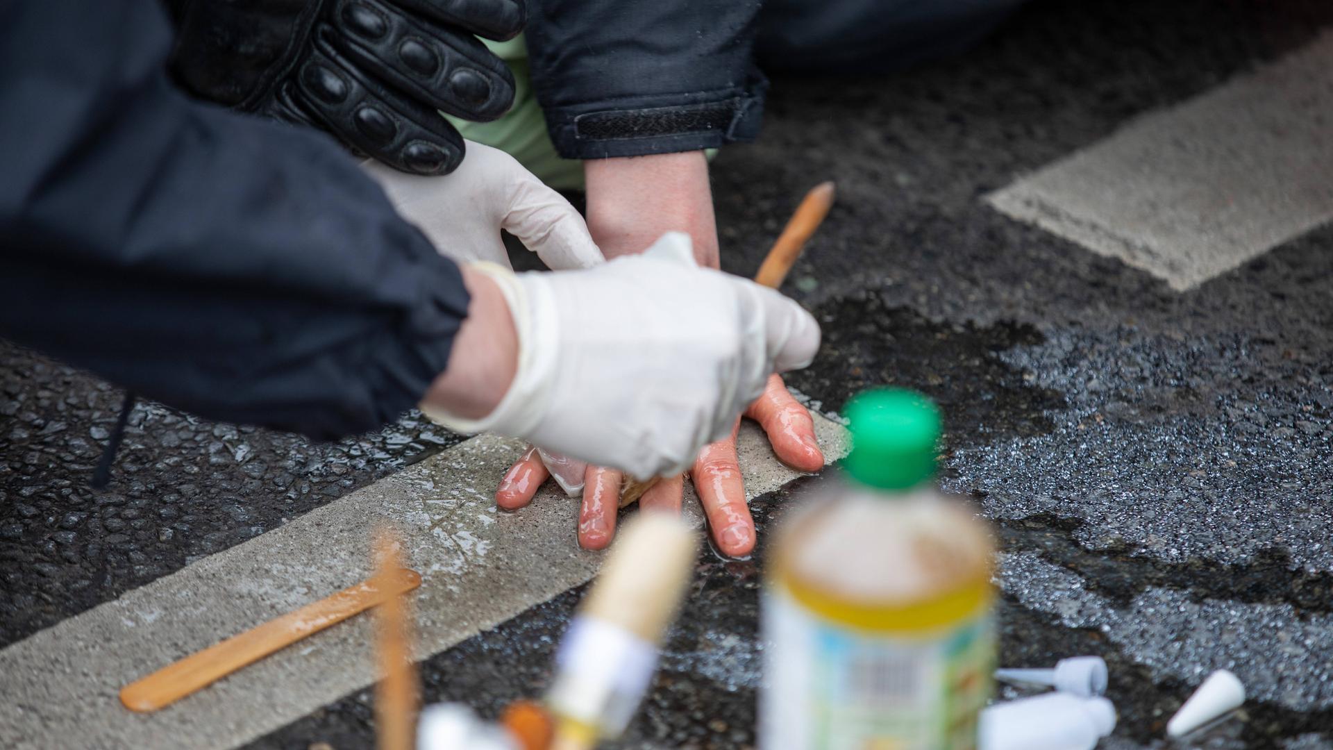 Klimaaktivisten blockieren eine Straße, indem sie sich mit Sekundenkleber an der Straße festkleben. Die Polizei löst sie mithilfe von Speiseöl. Klimaaktivisten blockieren eine Straße, indem sie sich mit Sekundenkleber an der Straße festkleben. Die Polizei löst sie mithilfe von Speiseöl.