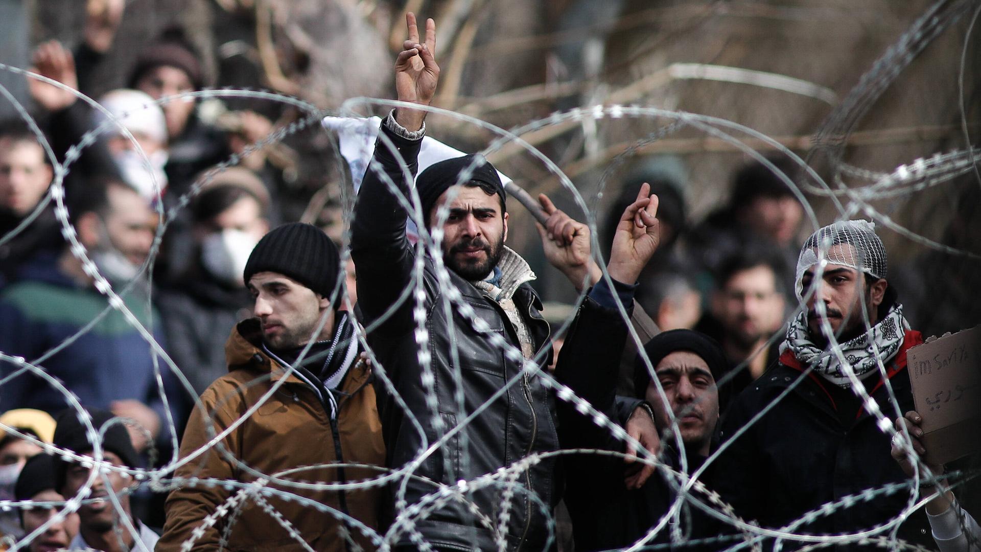 Migranten stehen hinter einem Maschendrahtzaun an der griechischen Grenze.