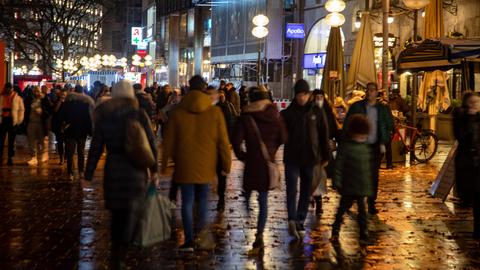 Viele Menschen sind am Abend auf einer Straße in einer Innenstadt unterwegs.