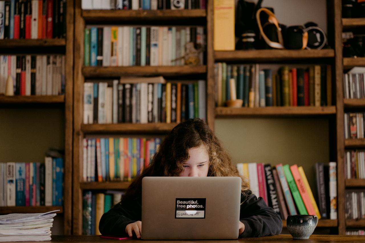Ein Mädchen sitzt halb versteckt hinter ihrem Laptop am Schreibtisch. Ein Mädchen sitzt halb versteckt hinter ihrem Laptop am Schreibtisch.