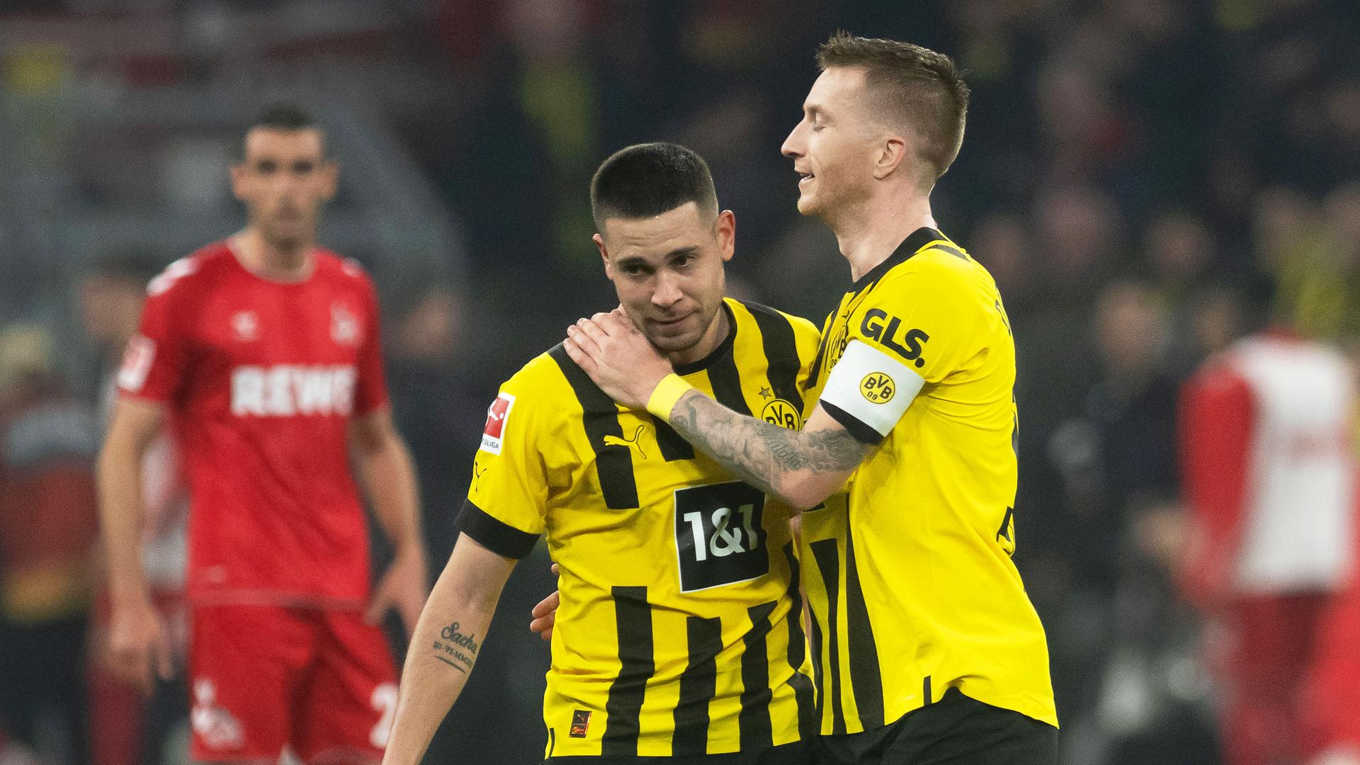Dortmunds Marco Reus (rechts) jubelt mit Teamkollege Raphael Guerreiro (Mitte) über seinen Treffer zum 3:0, im Hintergrund ist unscharf ein Spieler aus Köln zu sehen, der fassungslos den Jubelnden zuschaut. Dortmunds Marco Reus (rechts) jubelt mit Teamkollege Raphael Guerreiro (Mitte) über seinen Treffer zum 3:0, im Hintergrund ist unscharf ein Spieler aus Köln zu sehen, der fassungslos den Jubelnden zuschaut.