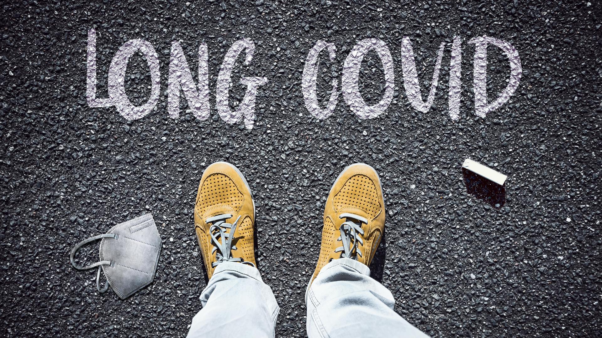 Person steht vor dem Schriftzug Long Covid Person steht vor dem Schriftzug Long Covid