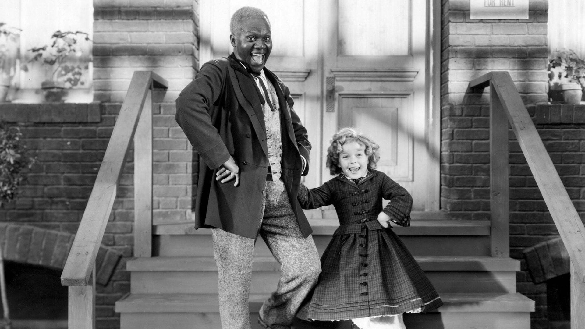 Bill Robinson und Shirley Temple stehen auf einer Treppe vor einem Haus Bill Robinson und Shirley Temple stehen auf einer Treppe vor einem Haus