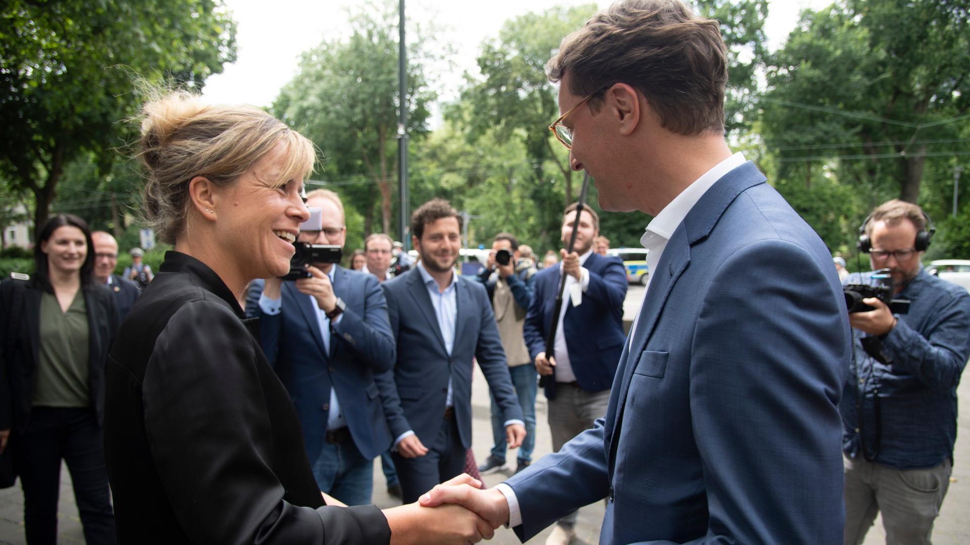 Auf dem Bild sieht man die Grünen-Chefin Mona Neubaur und Minister-Präsident Hendrik Wüst. Sie geben sich die Hand. 