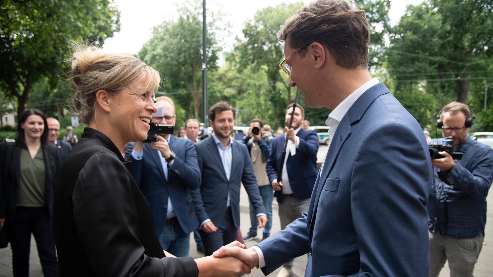 Auf dem Bild sieht man die Grünen-Chefin Mona Neubaur und Minister-Präsident Hendrik Wüst. Sie geben sich die Hand. Auf dem Bild sieht man die Grünen-Chefin Mona Neubaur und Minister-Präsident Hendrik Wüst. Sie geben sich die Hand.
