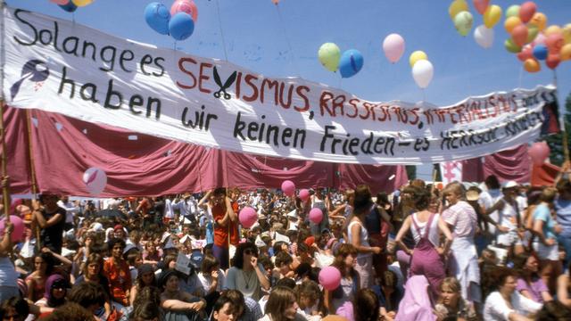 Friedensdemonstration 1982 in Bonn mit Transparent "Solage es Sexismus, Rassismus, Imperialismus gibt, haben wir keinen Frieden - es herrscht Krieg", darüber bunte Luftballons