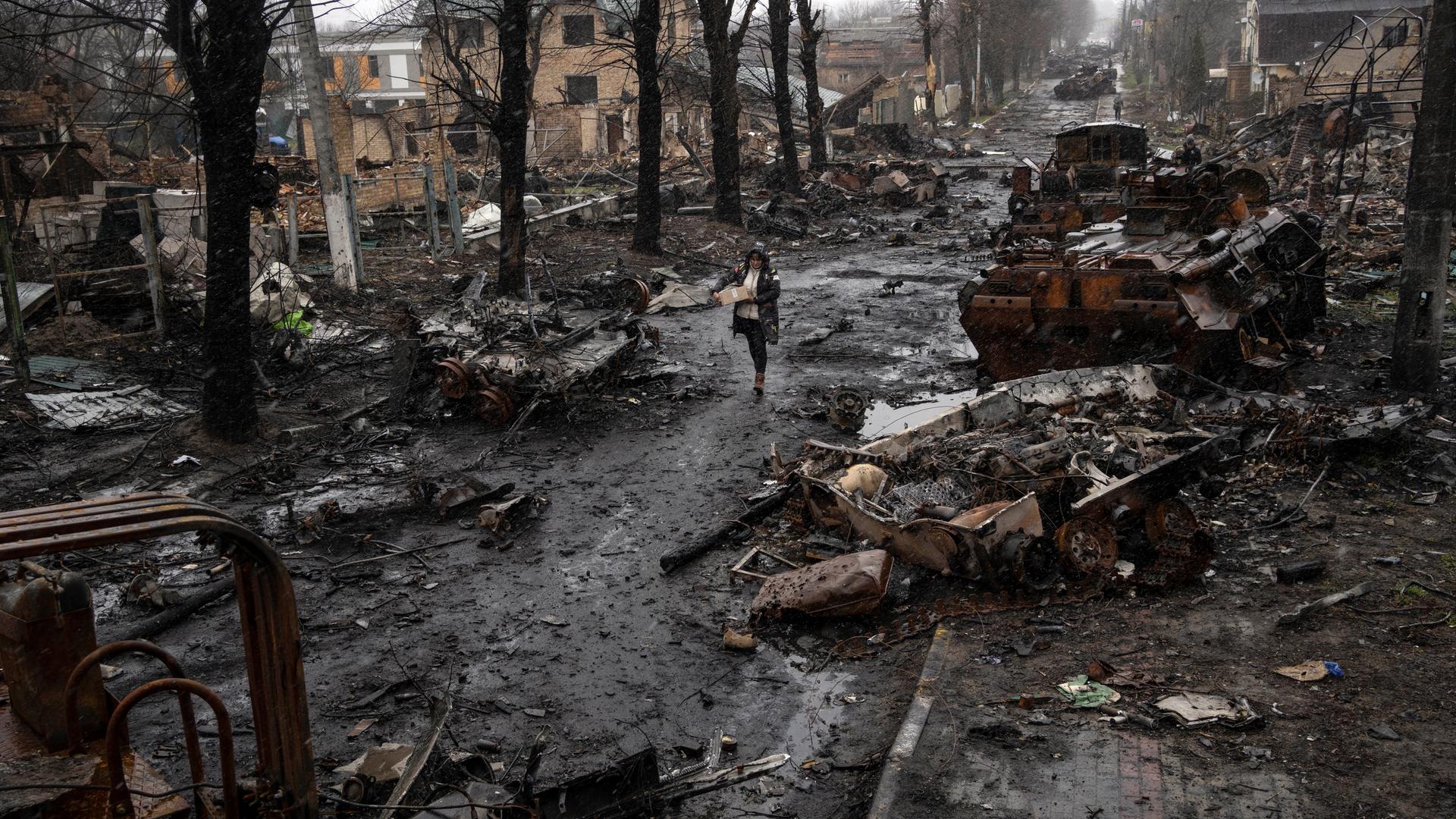 Eine Frau geht in Butscha auf einer Straße, die übersät ist mit zerstörten russischen Militärfahrzeugen. 