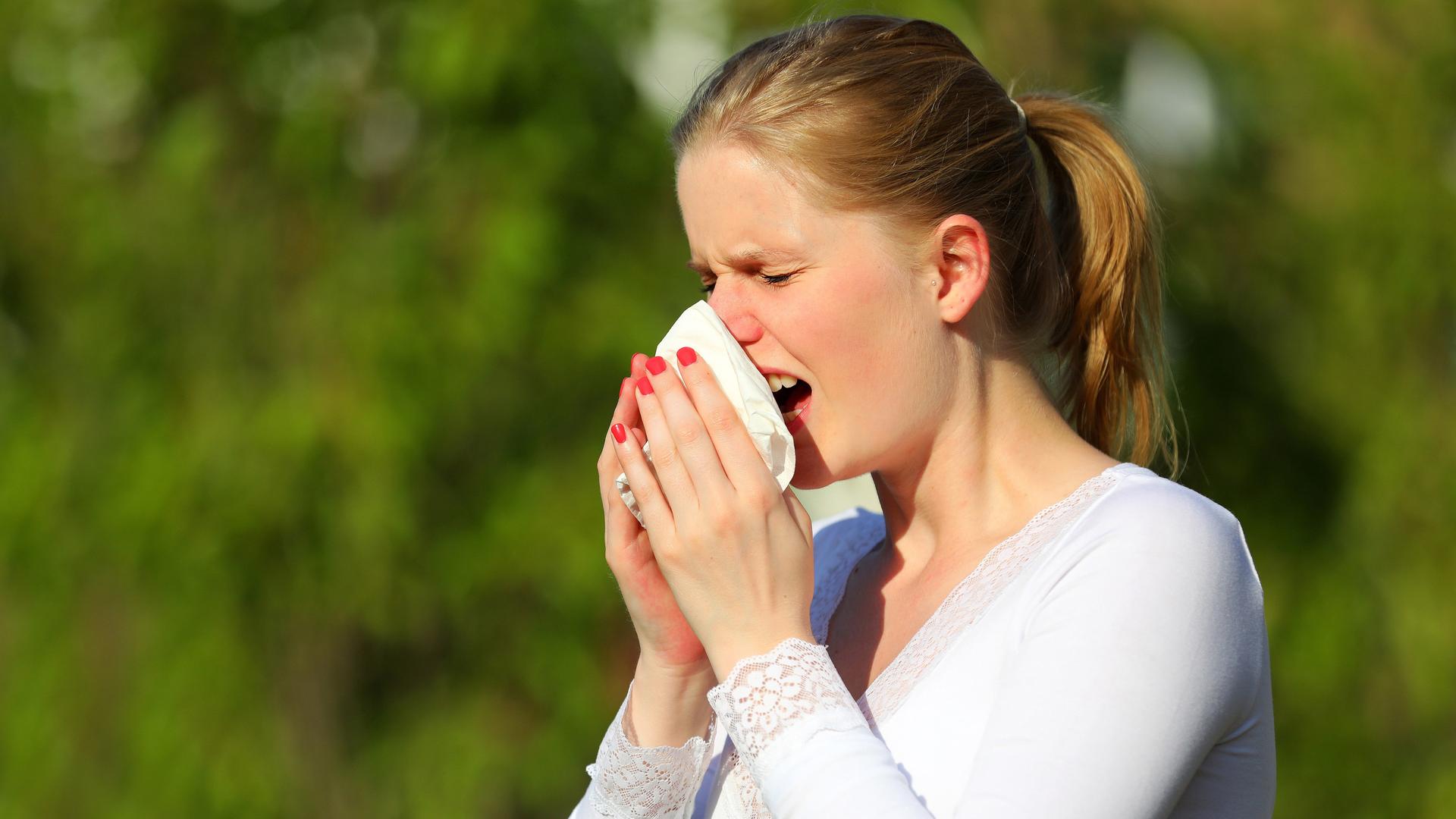 Eine junge Frau leidet unter Heuschnupfen und niest in ein Taschentuch.