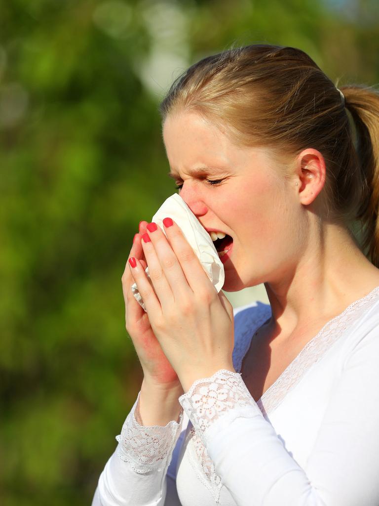 Eine junge Frau leidet unter Heuschnupfen und niest in ein Taschentuch.