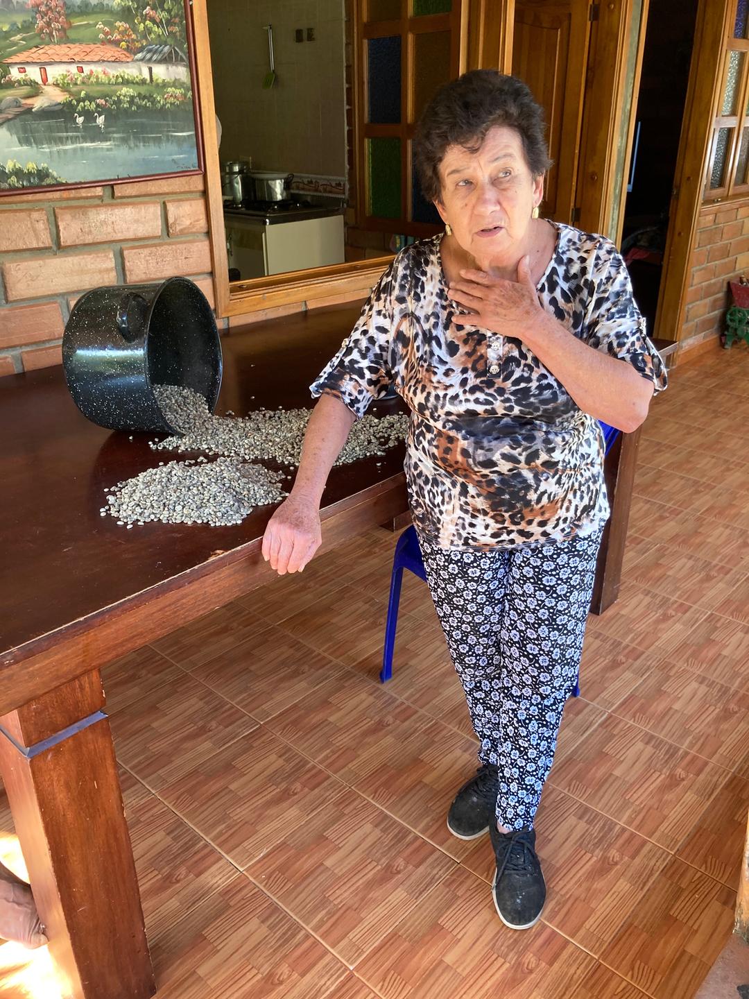 Eine ältere Dame steht neben einem Tisch, auf dem Kaffeebohnen ausgebreitet liegen.
