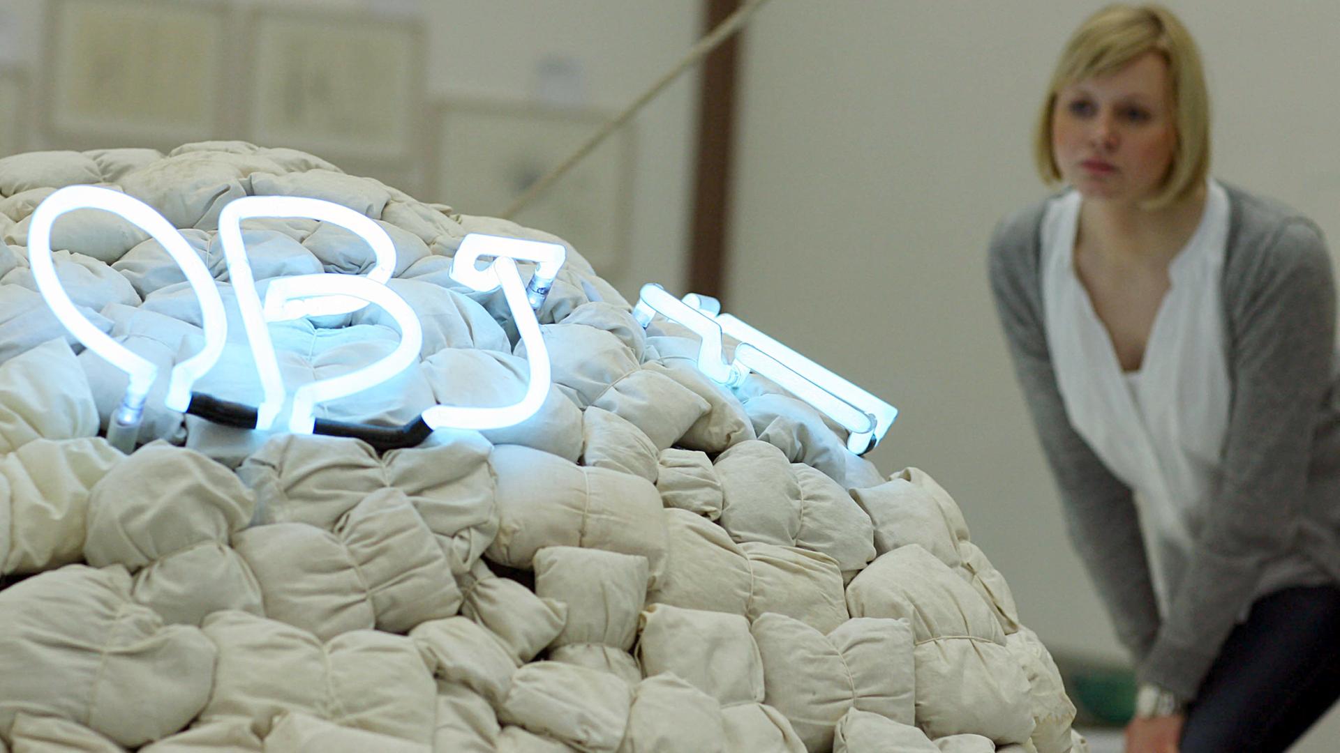 Eine Frau schaut auf ein Kunstwerk von Mario Merz mit dem Titel "Objet cache-toi" (Objekt versteck dich). Mit Holzwolle gefüllte Leichensäcke, die zu einem Iglu geformt sind. Eine Frau schaut auf ein Kunstwerk von Mario Merz mit dem Titel "Objet cache-toi" (Objekt versteck dich). Mit Holzwolle gefüllte Leichensäcke, die zu einem Iglu geformt sind.