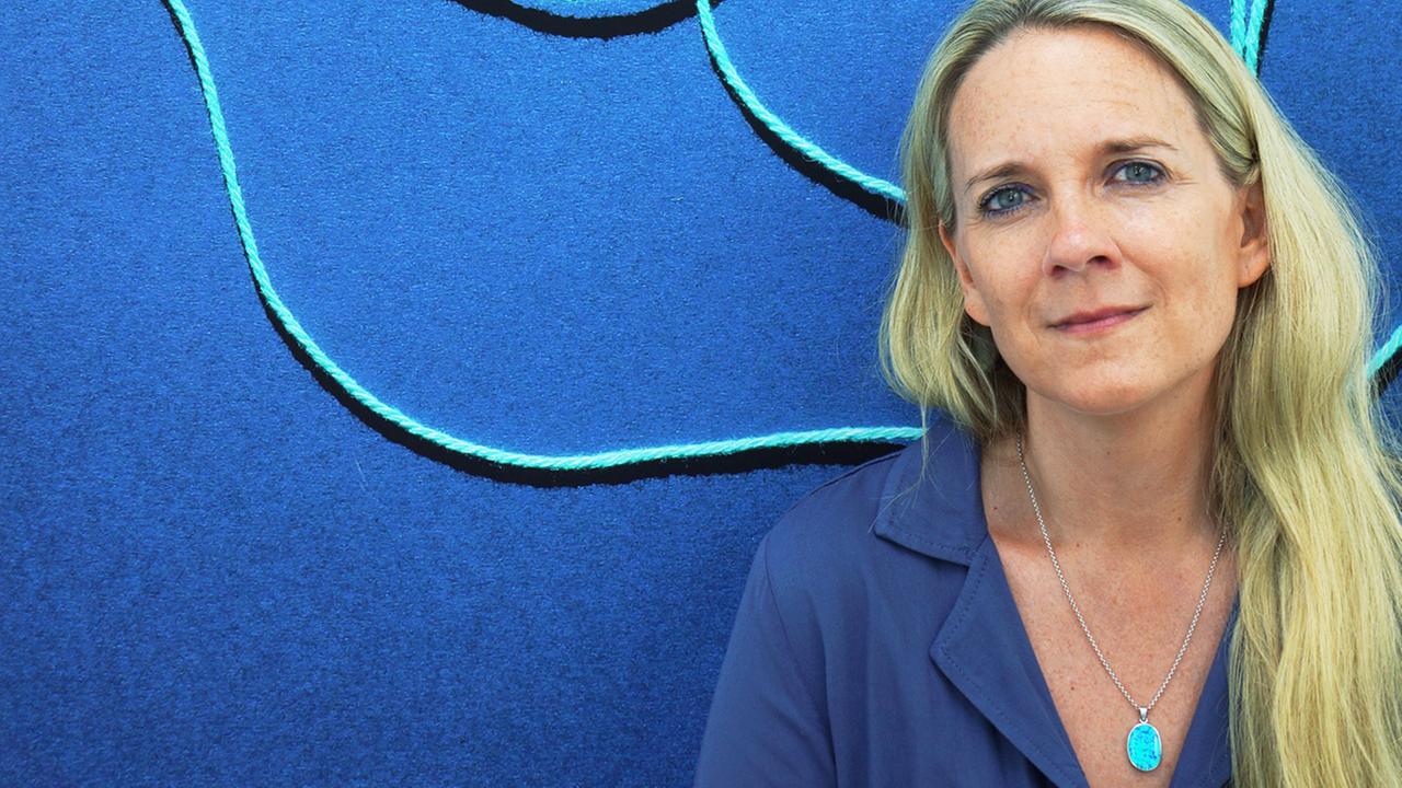 Fotografin Jessica Backhaus vor einem blauen Bild mit hellblauen Linien darin. Fotografin Jessica Backhaus vor einem blauen Bild mit hellblauen Linien darin.