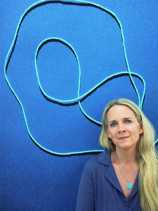 Fotografin Jessica Backhaus vor einem blauen Bild mit hellblauen Linien darin.