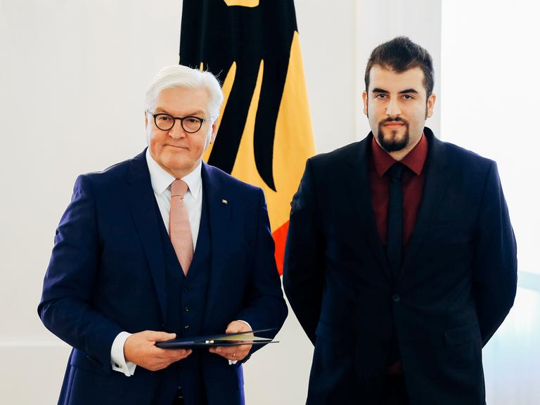 Bundespräsident Frank-Walter Steinmeier (L) überreicht Burak Yilmaz (R) das Bundesverdienstkreuz für sein Engagement gegen Antisemismus, die Zeremonie findet im Schloss Bellevue in Berlin statt.