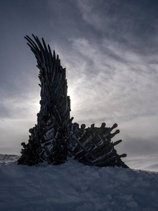 In einer düsteren Schneelandschaft steht der Thron aus der Fantasy-Serie Game of Thrones, daneben steckt ein Schwert im Schnee.