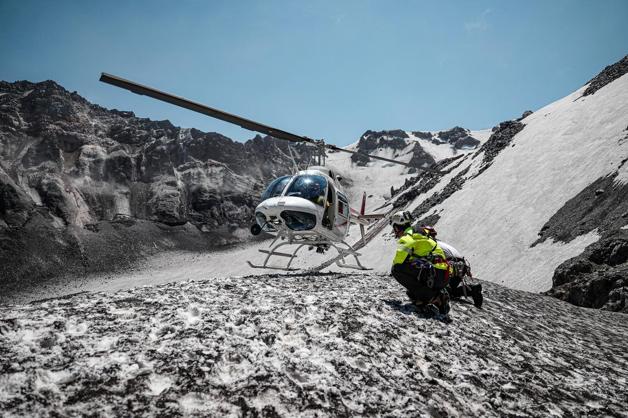 Helikopter landet in schneebedeckter Berglandschaft. Menschen stehen daneben. Helikopter landet in schneebedeckter Berglandschaft. Menschen stehen daneben.