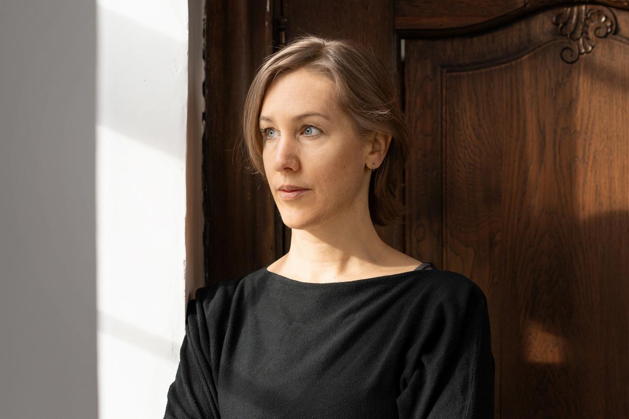 Portrait von Anna Yona, die zur Seite schauend vor einer Holztür steht. Portrait von Anna Yona, die zur Seite schauend vor einer Holztür steht.