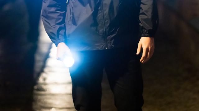 Ein Mann leuchtet nachts mit einer Taschenlampe auf einen Gehweg.