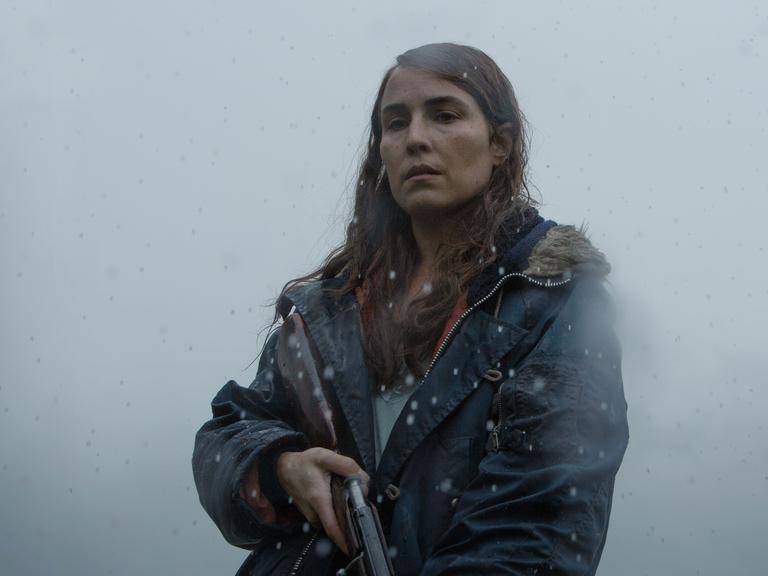 Hauptdarstellerin Noomi Rapace als Schafzüchterin Maria mit einem Gewehr in der Hand. Im Hintergrund wabert Nebel.
