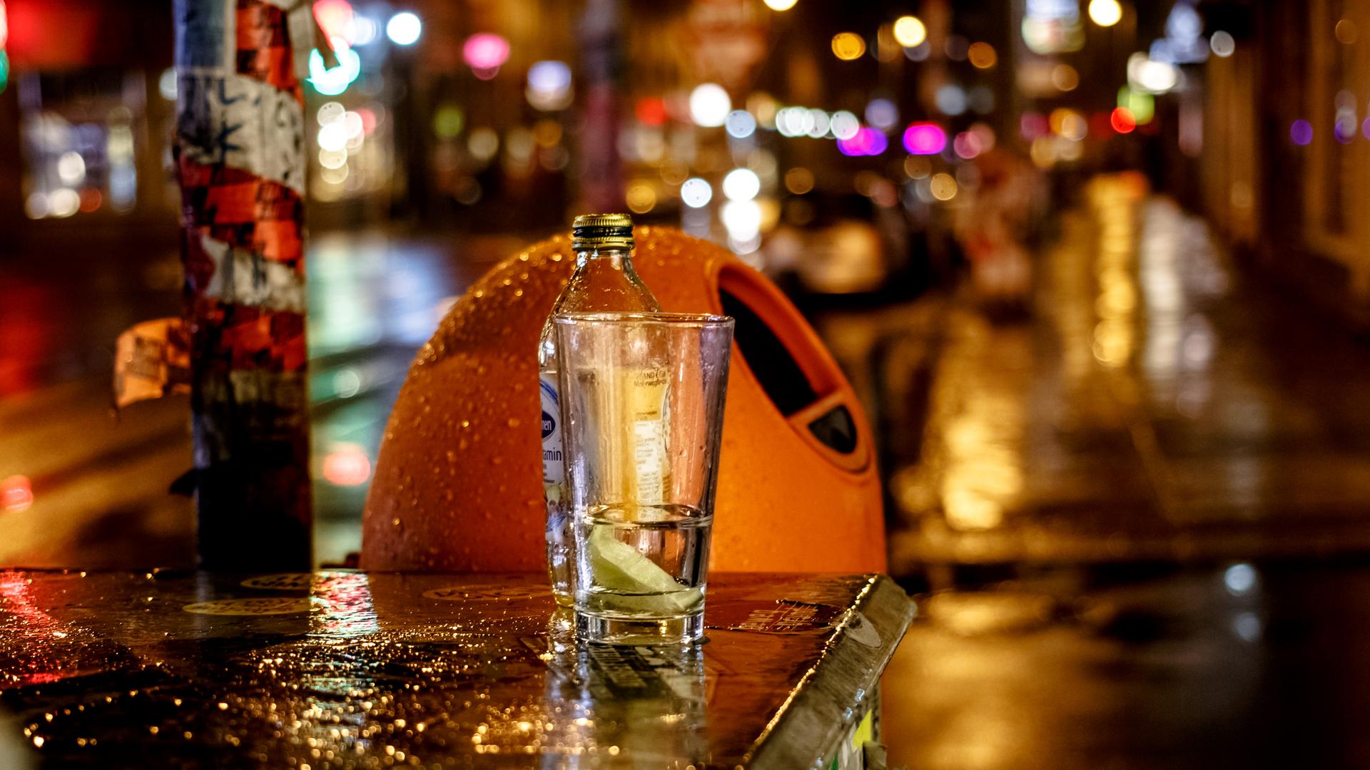 Nächtliche Straßenszene bei Regenwetter in Berlin. Zu sehen ist ein typischer orangefarbener Mülleimer. Davor, auf einem Kasten, steht eine Flasche und ein Glas. Nächtliche Straßenszene bei Regenwetter in Berlin. Zu sehen ist ein typischer orangefarbener Mülleimer. Davor, auf einem Kasten, steht eine Flasche und ein Glas.