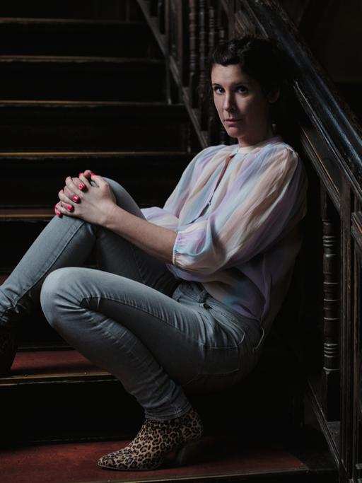 Die Autorin Daniela Droescher sitzt auf der Treppe eines Hausaufgangs und lehnt an das Geländer.