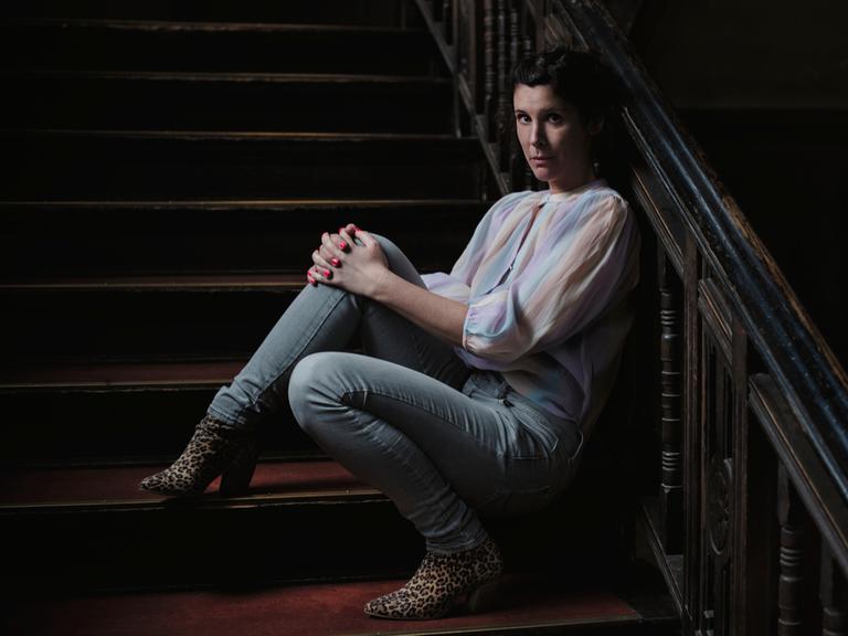 Die Autorin Daniela Droescher sitzt auf der Treppe eines Hausaufgangs und lehnt an das Geländer.
