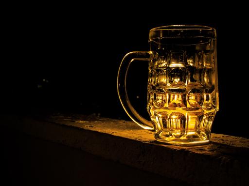 Ein leerer Bierkrug aus Glas vor einem schwarzen Hintergrund wird golden angeleuchtet.