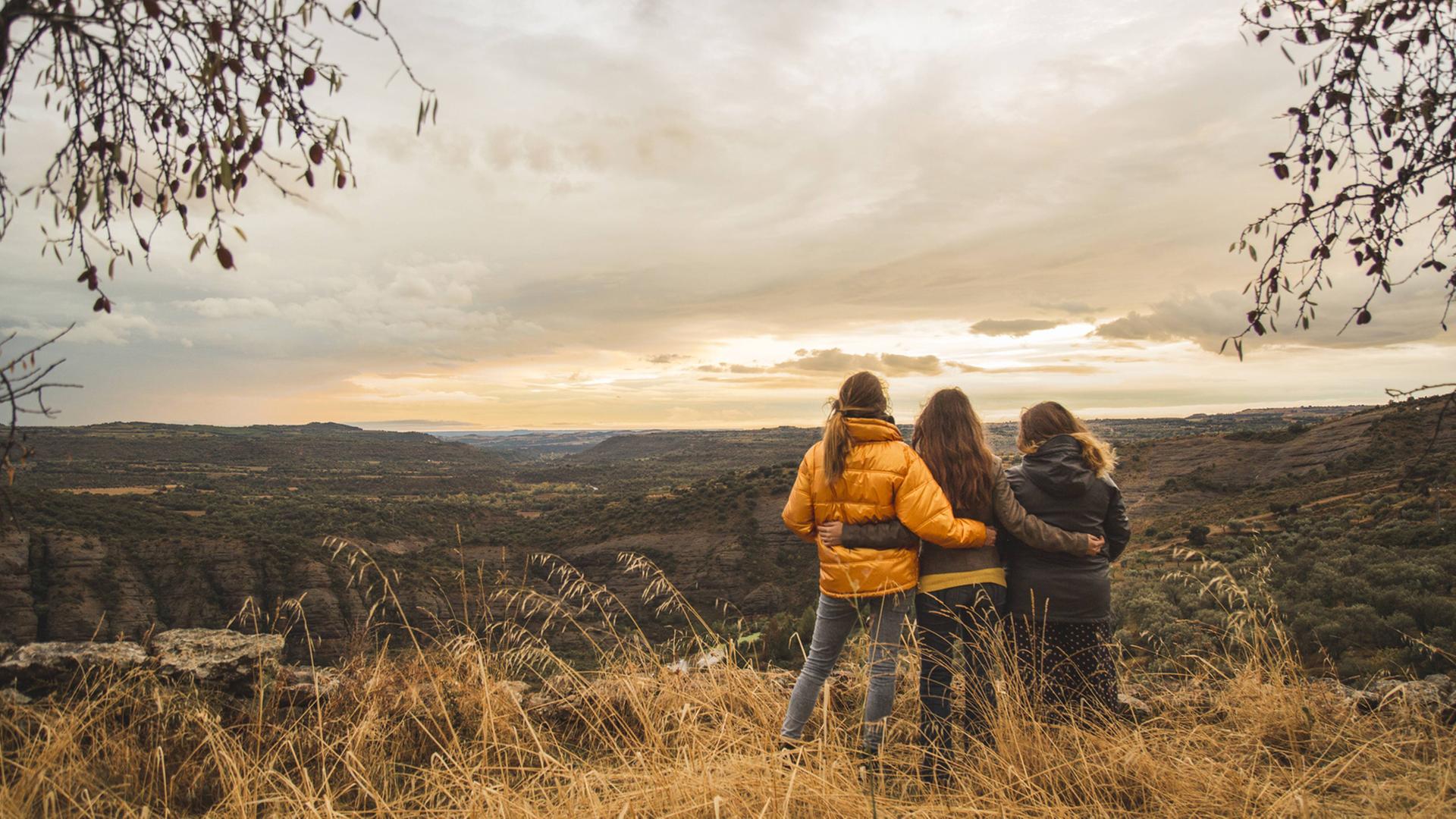 Drei junge Frauen sind mit dem Rücken zur Kamera zu sehen und stehen in der Landschaft. Drei junge Frauen sind mit dem Rücken zur Kamera zu sehen und stehen in der Landschaft.