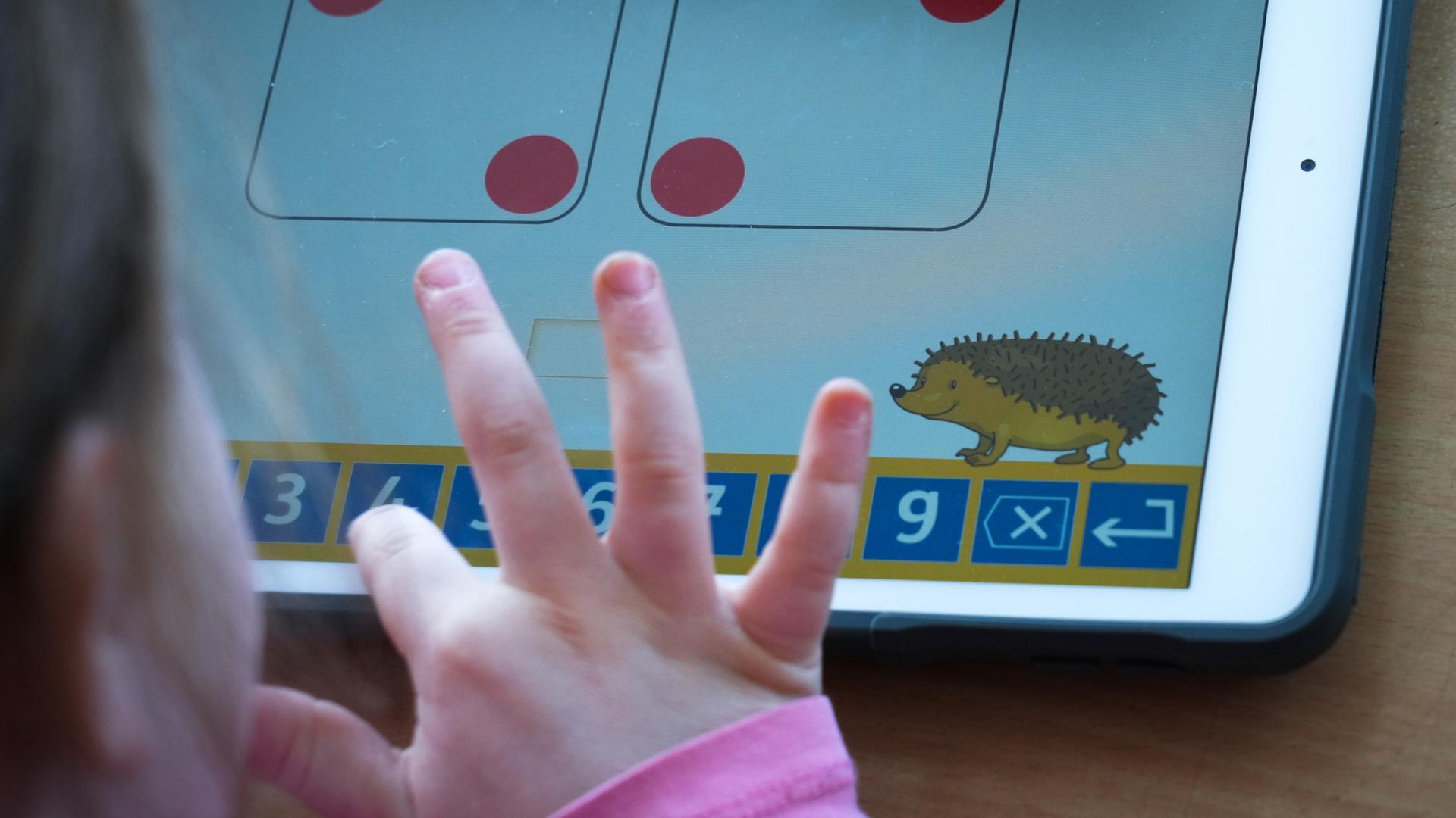 Kinderfinger tippen auf einem Tablet auf dem spielerisch eine Rechenaufgabe dargestellt ist.