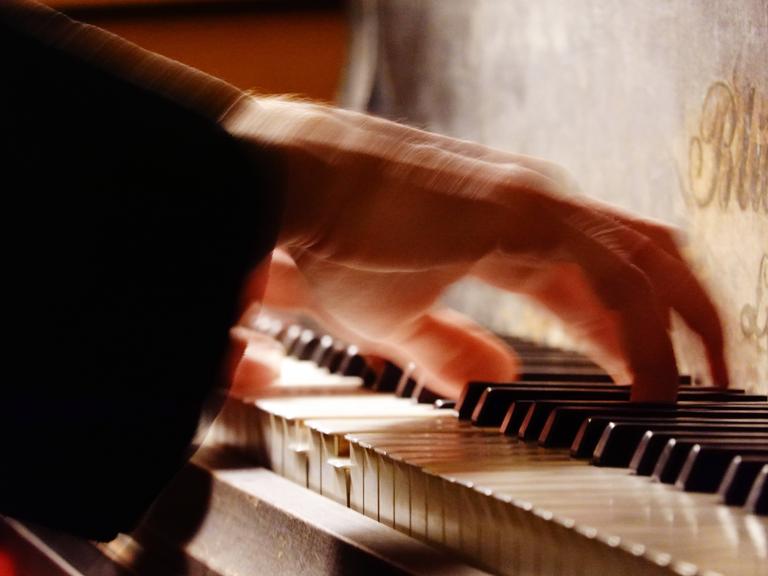 Eine sich bewegende Hand gleitet über die Tasten eines Flügels. 